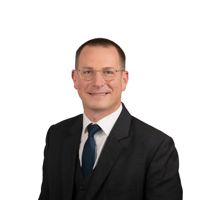Max Allendorf, Rechtsanwalt, lächelt freundlich im dunklen Anzug mit Krawatte und runder Brille.