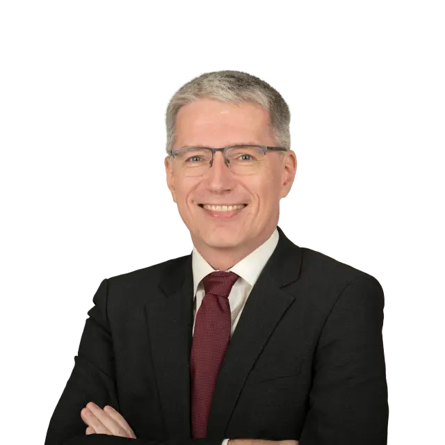Anwalt Thomas Hänsch lächelt im dunklen Anzug mit Krawatte und verschränkten Armen.