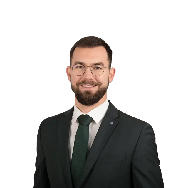 Porträt von Rechtsanwalt Marc Henschel im dunklen Anzug mit grüner Krawatte und runder Brille.