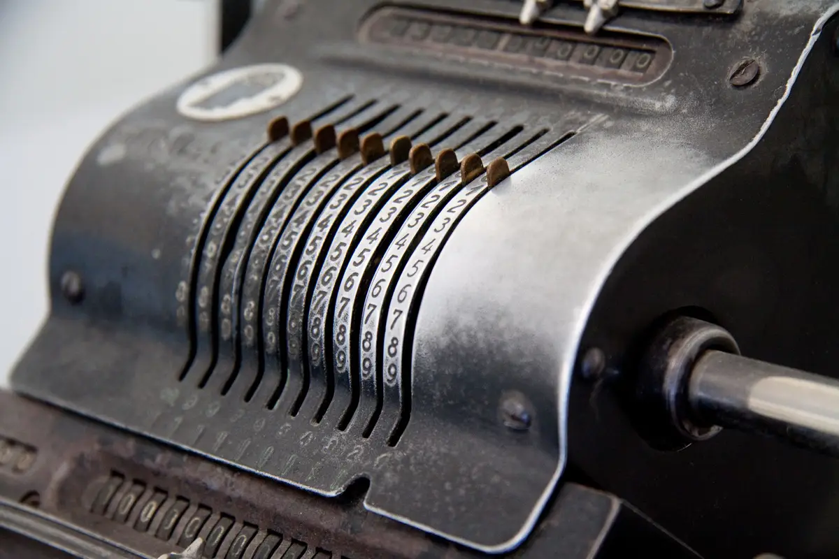 Nahaufnahme einer historischen mechanischen Rechenmaschine mit Ziffernwalzen und Kurbel.