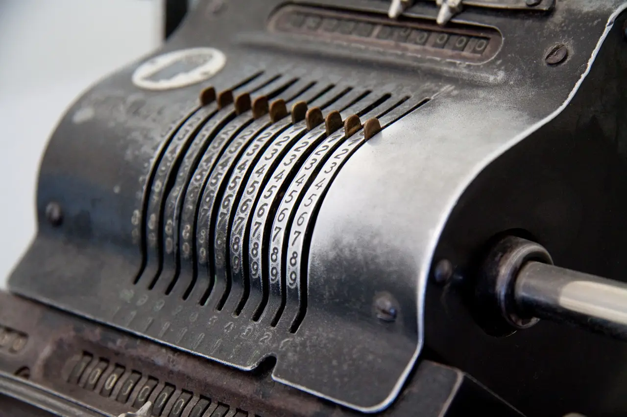 Nahaufnahme einer historischen mechanischen Rechenmaschine mit Ziffernwalzen und Kurbel.