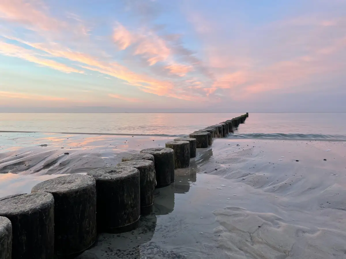 Reihe von Holzpfählen im flachen Wasser bei Sonnenuntergang am Strand