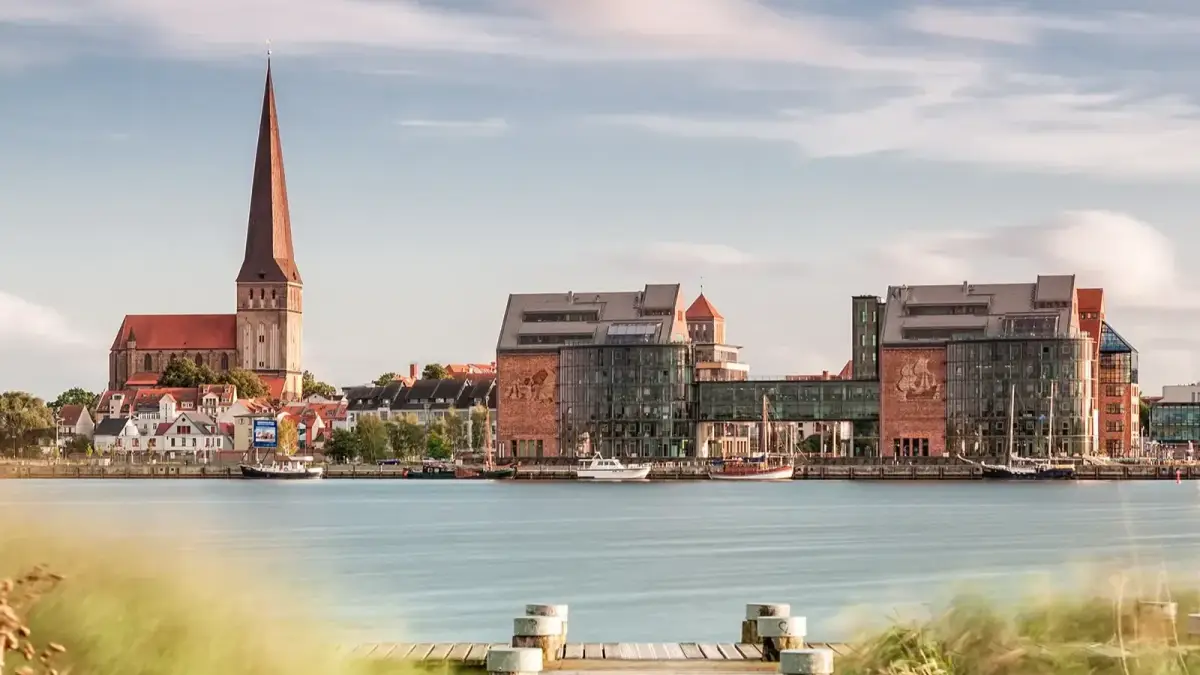 Panorama von Rostock mit Kirche, moderner Hafenarchitektur und Booten am Wasser.