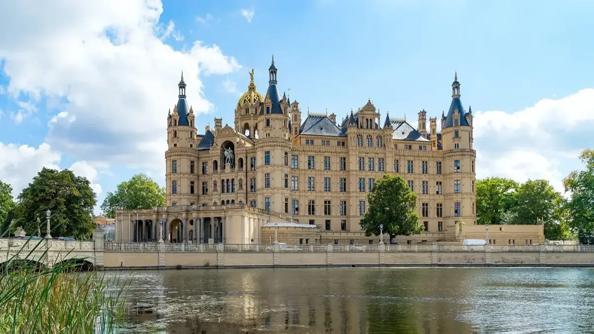 Schweriner Schloss mit Türmen und goldenem Dach am Wasser unter blauem Himmel.